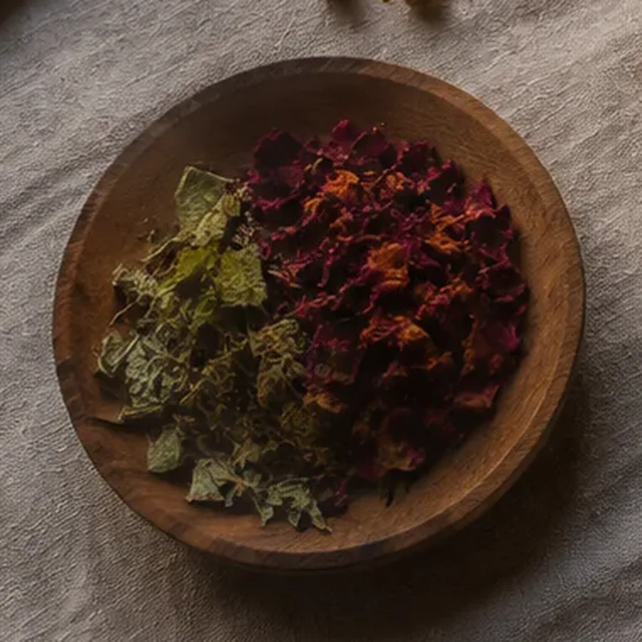 Coupelle en bois remplie de pétales de rose et de feuilles séchées posée sur une nappe de lin